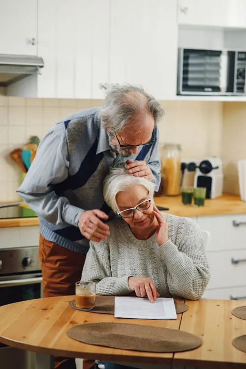 Adult child writing notes at a kitchen table with printed care planning documents