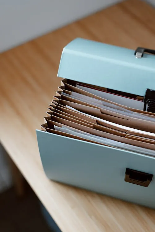 Teal accordion file box with organized folders on a wooden desk, ready for important documents