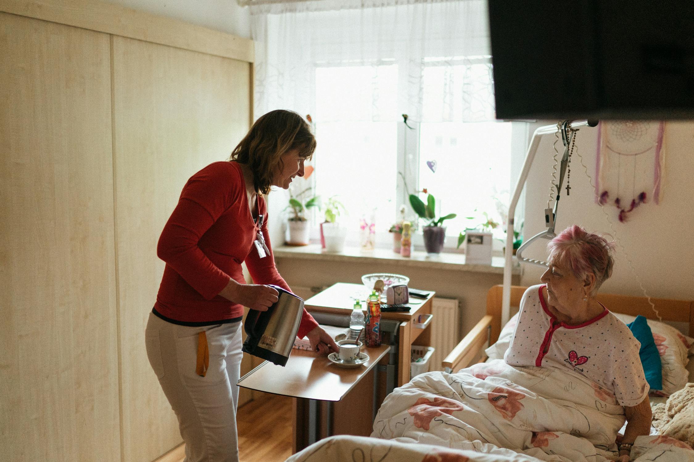 Caregiver serving tea to an elderly woman in a cozy setting, both sharing a warm moment