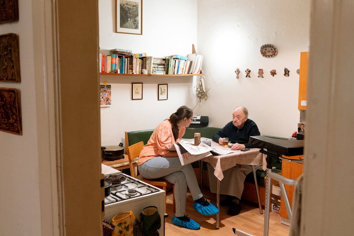 Adult child and aging parent sitting together in a warm home, talking over coffee in a relaxed and connected moment