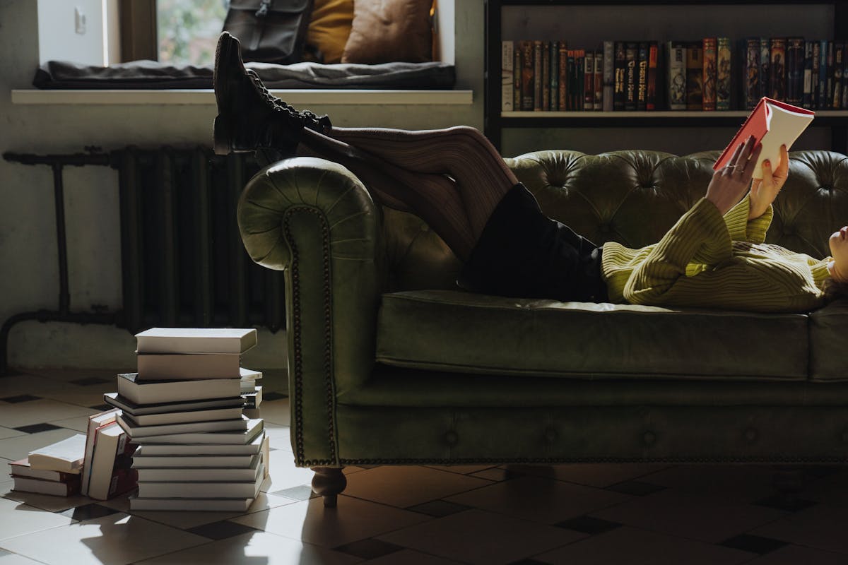 Person lying on a couch reading a book, afternoon light through the window, genuinely resting