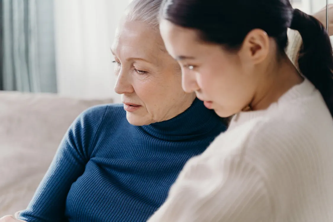Elderly mother and adult daughter in quiet, attentive conversation side by side at home