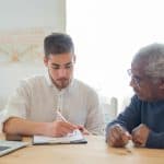 Adult child helping elderly parent with financial paperwork at home