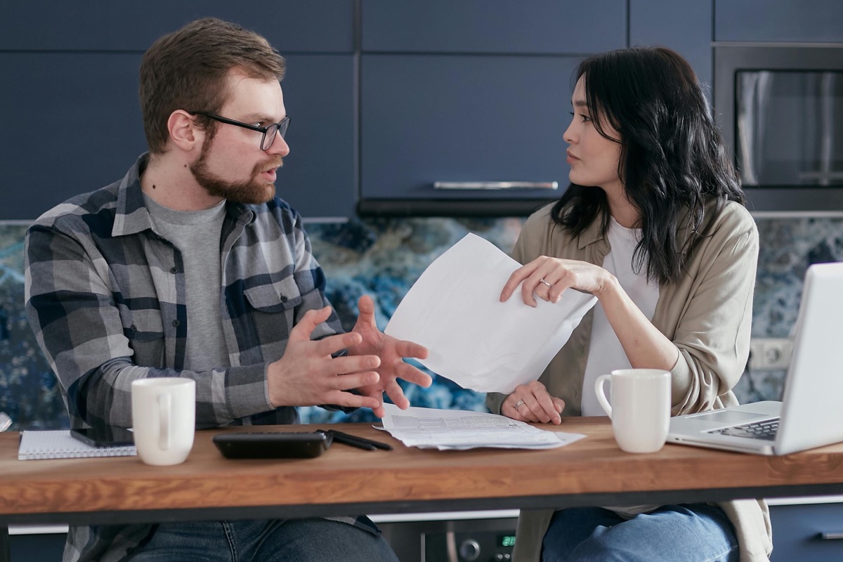 Two adult siblings at a kitchen table reviewing documents and discussing their aging parent