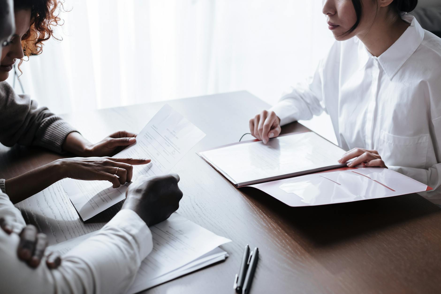 Two people at a table in a professional setting, one passing a folder to the other