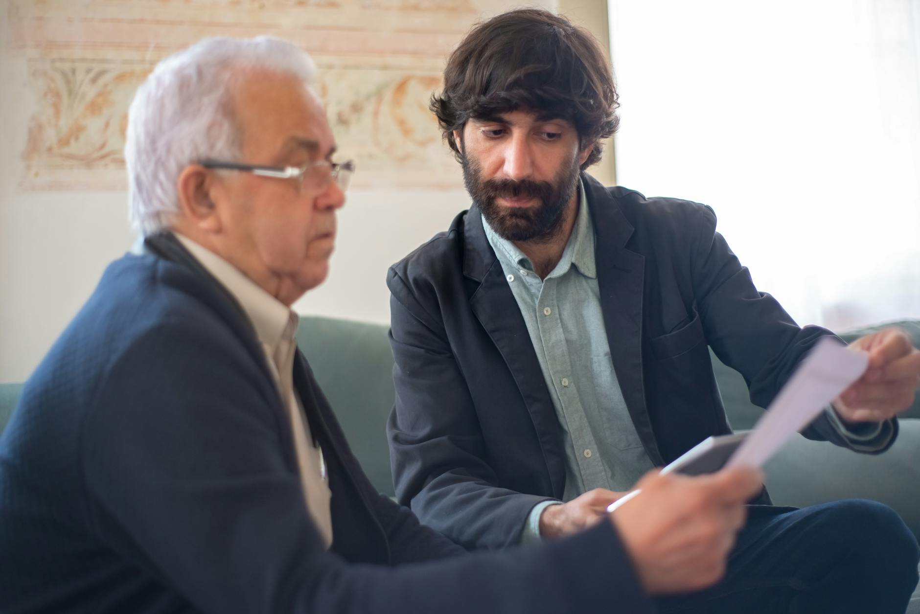 Adult child and aging parent sitting together at a kitchen table reviewing printed materials